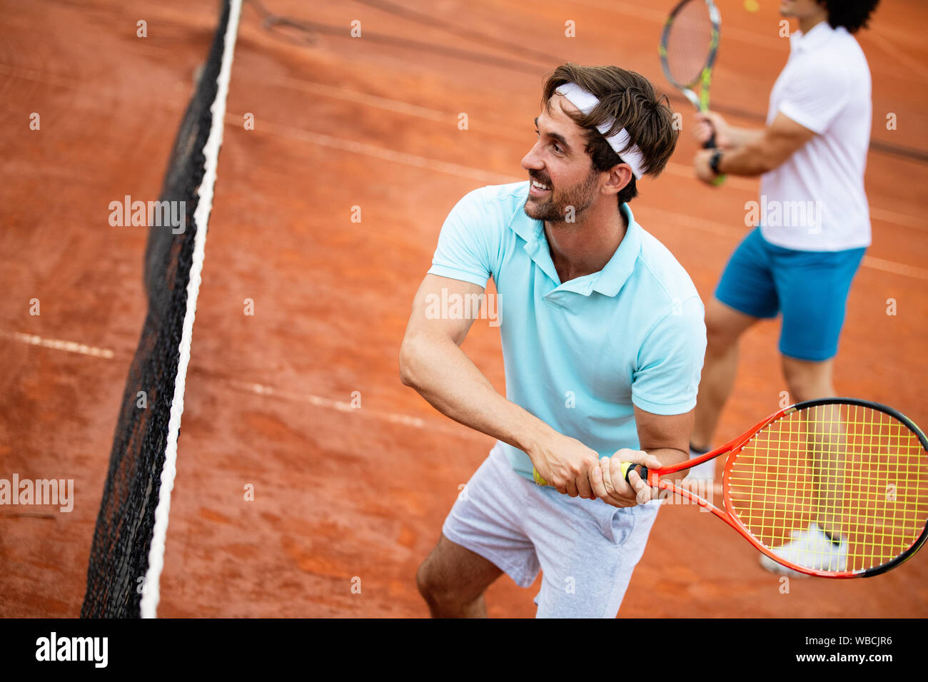 Immagine del bel giovane sul campo da tennis. L'uomo gioca a tennis. L'uomo gettando palla da tennis. Bellissima zona di foresta come sfondo Foto Stock