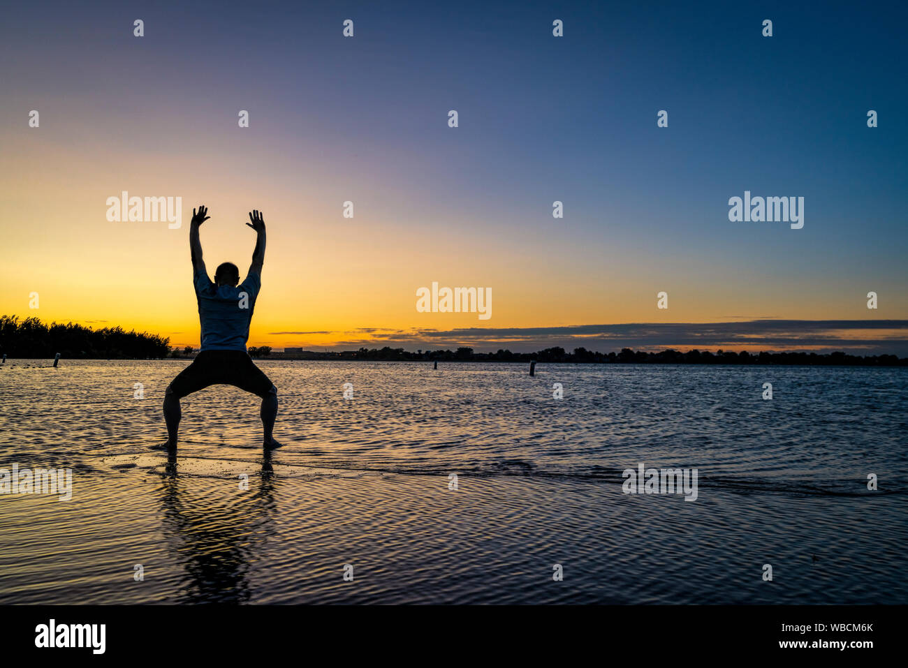 Sunrise silhouette di un uomo in piedi in acqua poco profonda e la pratica di chigong o tai chi movimenti, Boyd il lago del Parco statale nel nord del Colorado Foto Stock