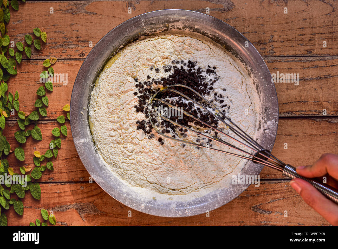 Ciotola con gli ingredienti necessari per preparare una torta con scaglie di cioccolato su una superficie in legno Foto Stock