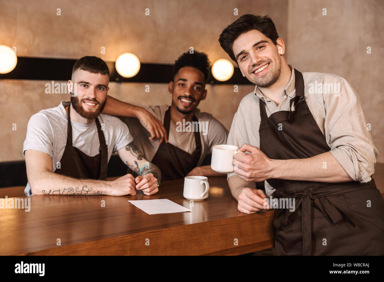 Tre uomini allegra baristi presso la caffetteria, bere il caffè durante la pausa Foto Stock