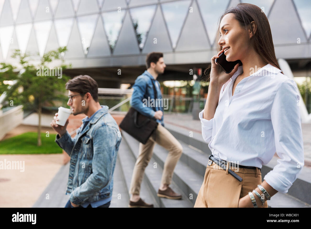 In prossimità di una giovane e bella donna asiatica parlando al telefono cellulare mentre si cammina giù per le scale al via della città circondato dalla folla Foto Stock