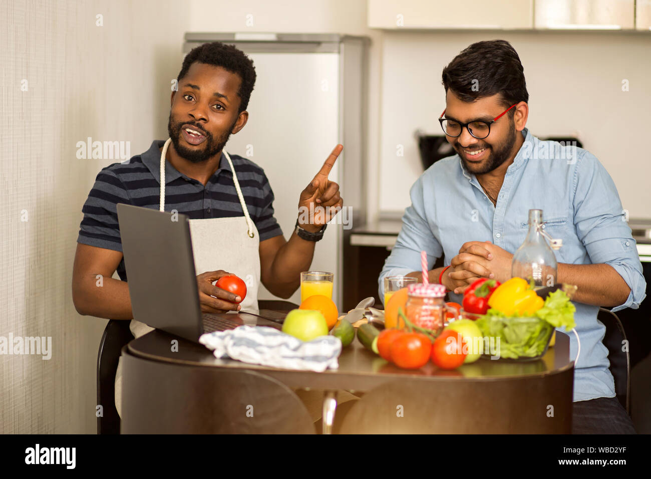 Bello stupiti americano africano giovane puntando con il dito al suo amico indiano che andare a cucinare e sorridente. Gioiosa multi etnico sitti studenti Foto Stock