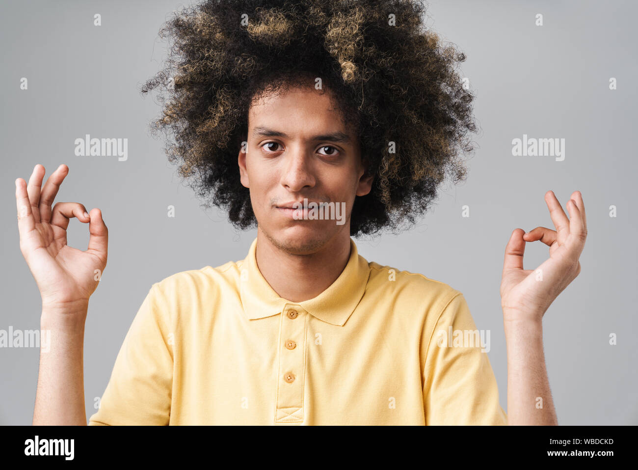 Foto di rilassante uomo caucasico con acconciatura afro meditando e mantenendo le dita nel gesto zen isolate su uno sfondo grigio Foto Stock