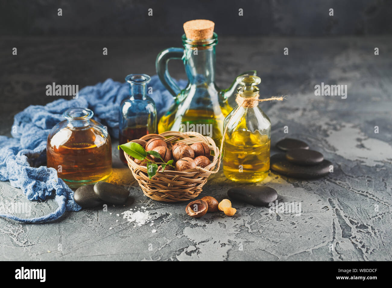 Bottiglie di vetro con naturale olio di macadamia con noci macadamia, sale marino e pietre zen. Super e cibo sano concetto Foto Stock