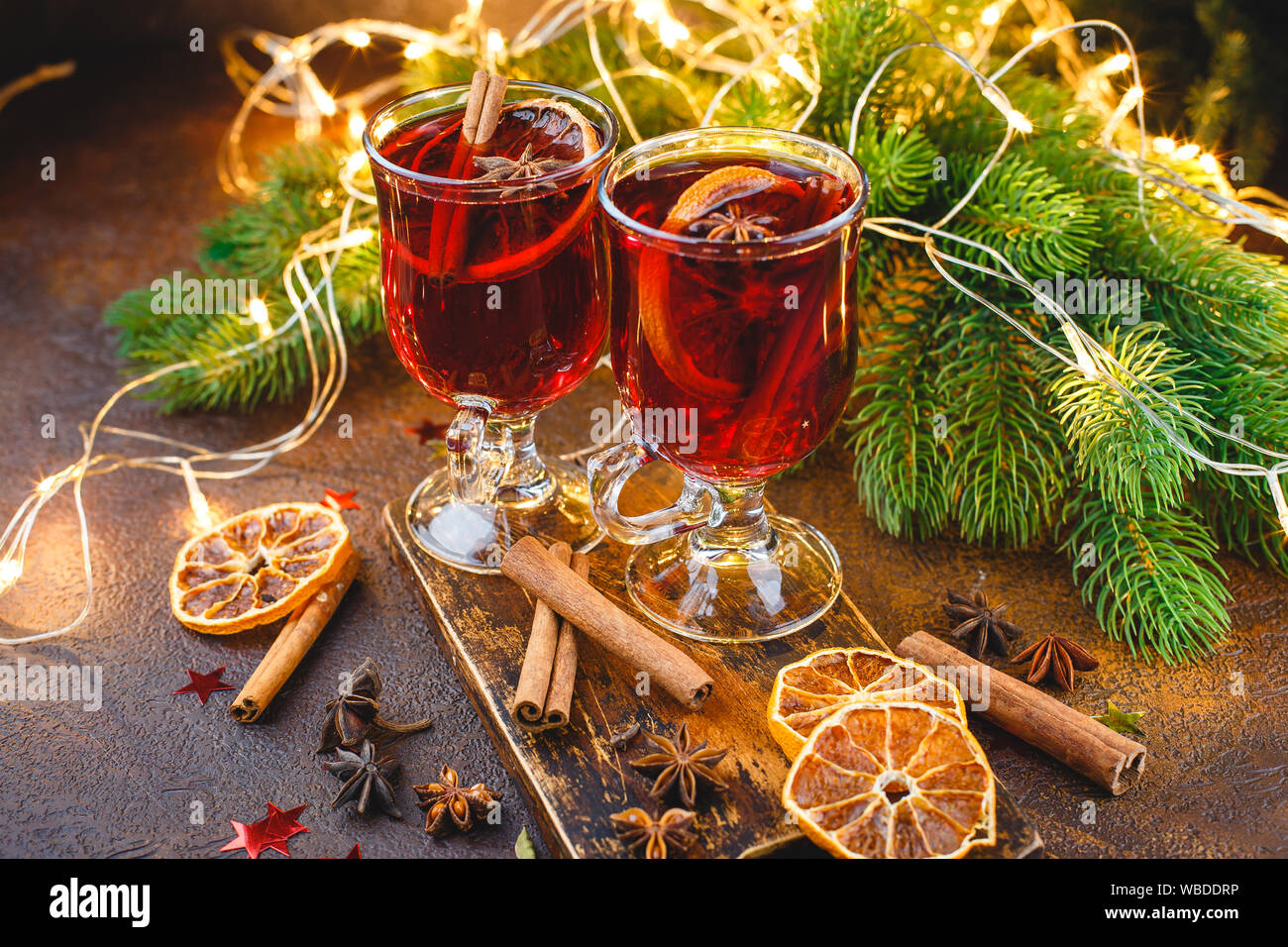 Le coppe di vetro di vin brulé con spezie e arancio secco di pezzi sul tagliere di legno su sfondo scuro. Tradizionale bevanda di Natale Foto Stock