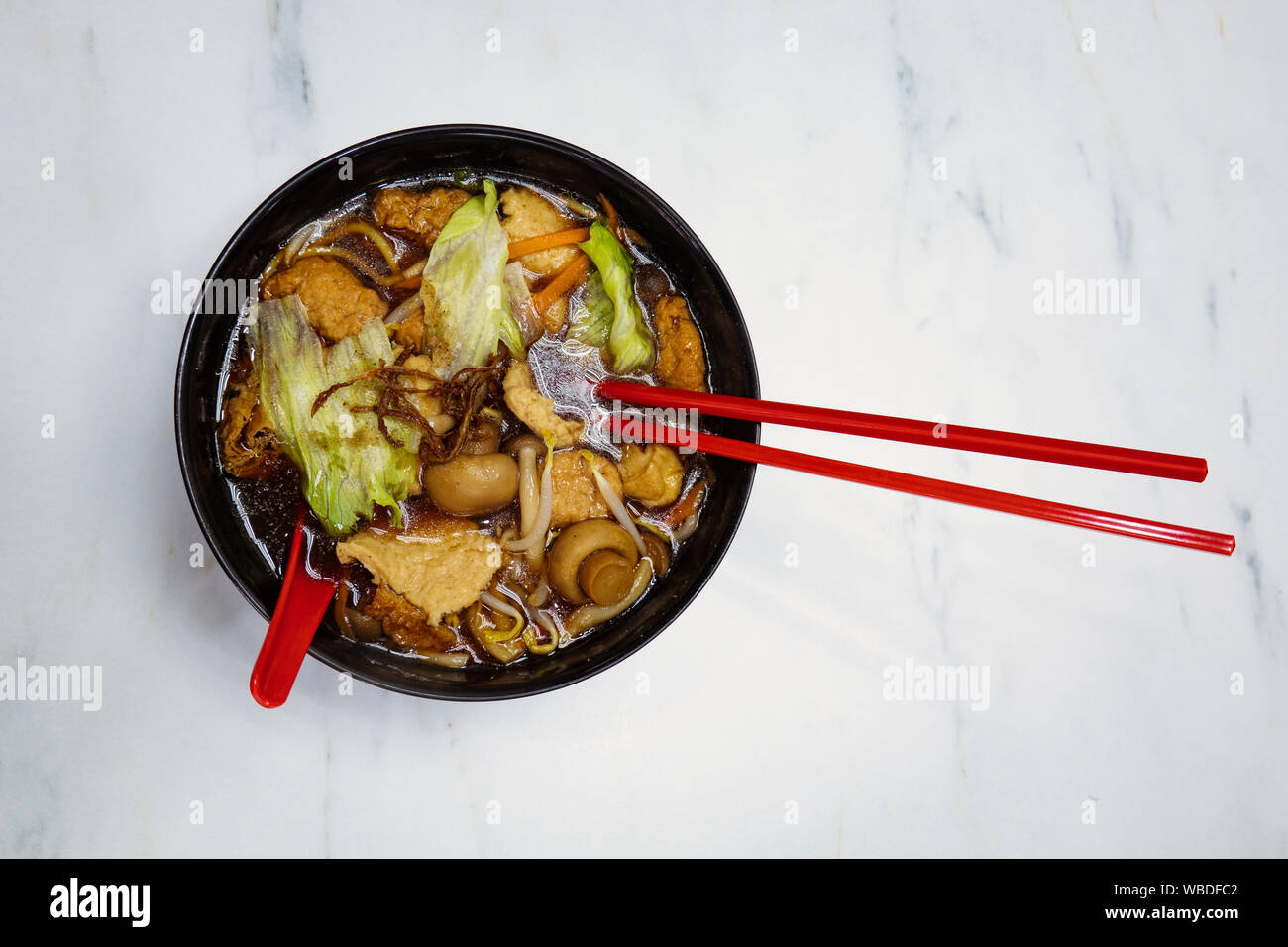 Un fungo vegana e tofu a base di noodle asiatici minestra chiaro, servita in una ciotola nero con rosso bacchette in un ristorante a Singapore. Foto Stock