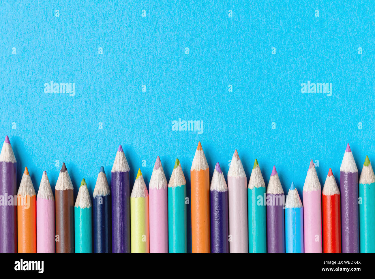 Confine di matite colorate contro un blu brillante background testurizzato. Torna a scuola con il concetto di spazio di copia Foto Stock