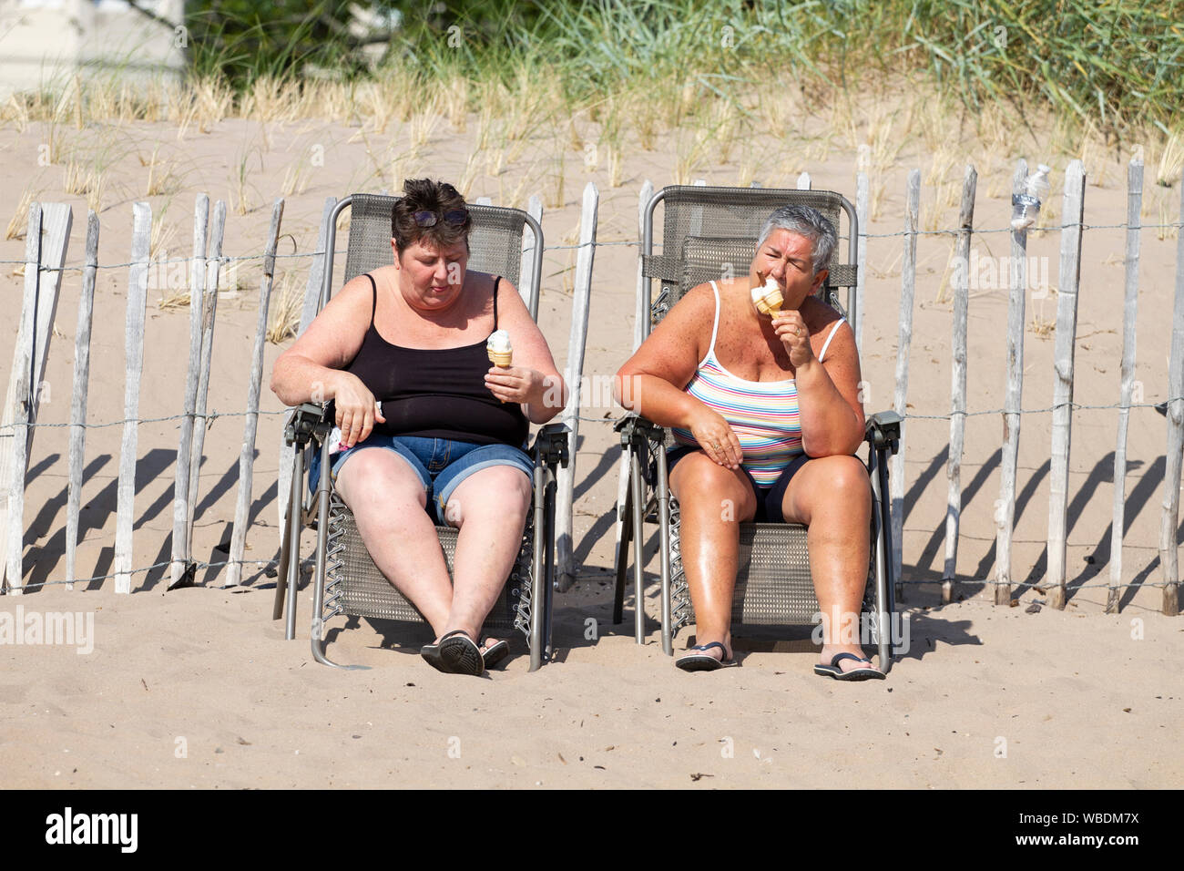 Dundee, Tayside, Scotland, Regno Unito. 26 Agosto, 2019. Regno Unito: meteo ondata di caldo spazza Dundee su lunedì festivo con temperature che raggiungono i 24º Celsius. Vacanzieri godere del tardo pomeriggio meteo su Broughty Ferry beach. Due donne seduti sui sedili di raffreddamento di mangiare il gelato coni . Credito: Dundee fotografico / Alamy Live News Foto Stock