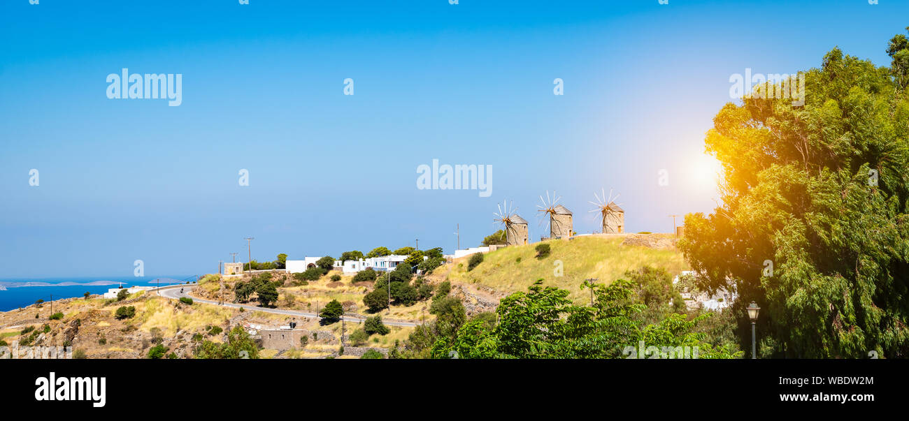 Paesaggio panoramico vista di Patmos isola al tramonto con tre mulini a vento sulla collina contro il cielo blu sullo sfondo di un giorno d'estate. Foto Stock