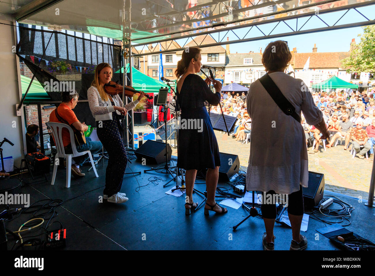 Sandwich e folk festival Ale. Vista dal retro dello stadio di francese irlandese folk gruppo, Rileanna, sul palco di fronte seduto in udienza in piazza del mercato. Foto Stock