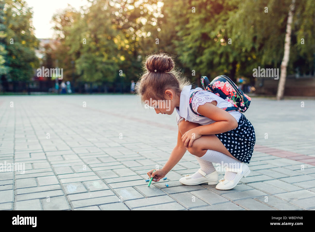 Felice bambina indossa uno zaino e disegno con chalk all'esterno la scuola primaria. Kid divertirsi dopo le classi. Si torna a scuola Foto Stock