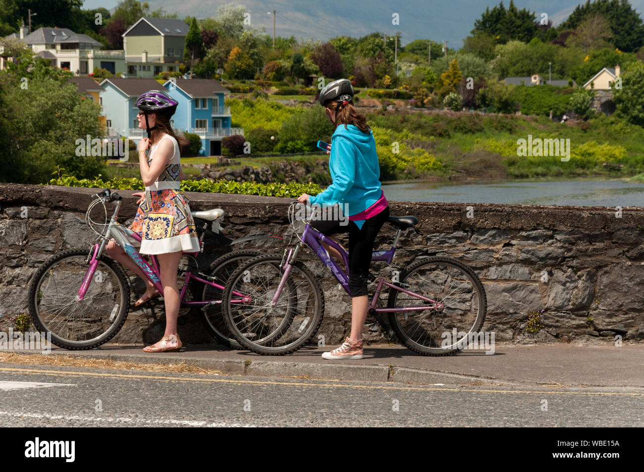 Ciclismo in Irlanda. Turisti femminili con biciclette godersi una giornata fuori sul N70 Ring of Kerry Road al Killorglin River Laune Bridge, County Kerry, Irlanda Foto Stock