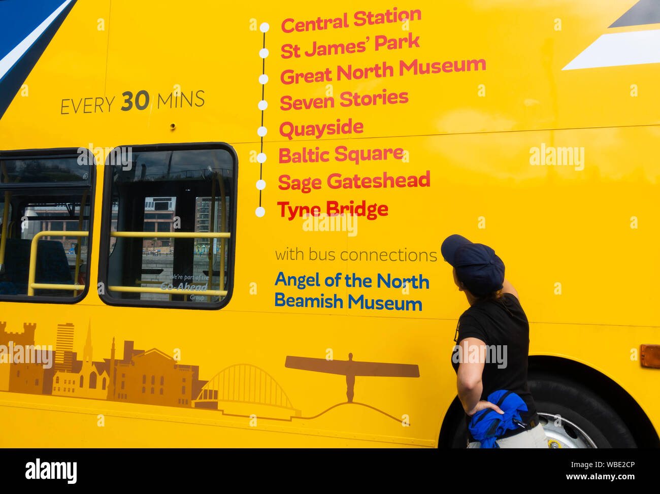 Turista femminile accanto a/Newcastle Gateshead open top tour bus. Newcastle upon Tyne, Inghilterra. Regno Unito Foto Stock