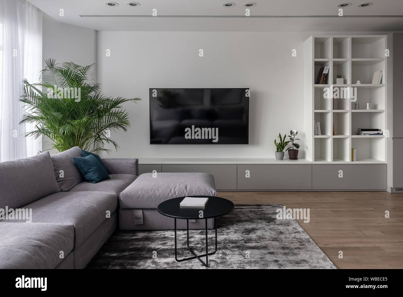 Interno in uno stile moderno con pareti bianche e pavimenti in parquet con  un tappeto sul pavimento. Vi è un divano grigio con cuscini, round table  nero, piano verde Foto stock -