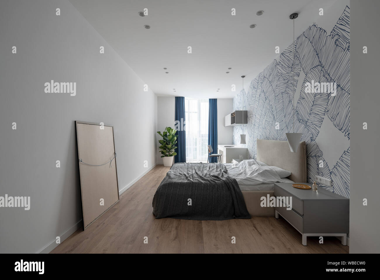 Camera da letto in stile moderno con pareti bianche con modelli e un pavimento in parquet. Vi è un letto matrimoniale, comodini grigio, tavolo luminoso con una sedia Foto Stock
