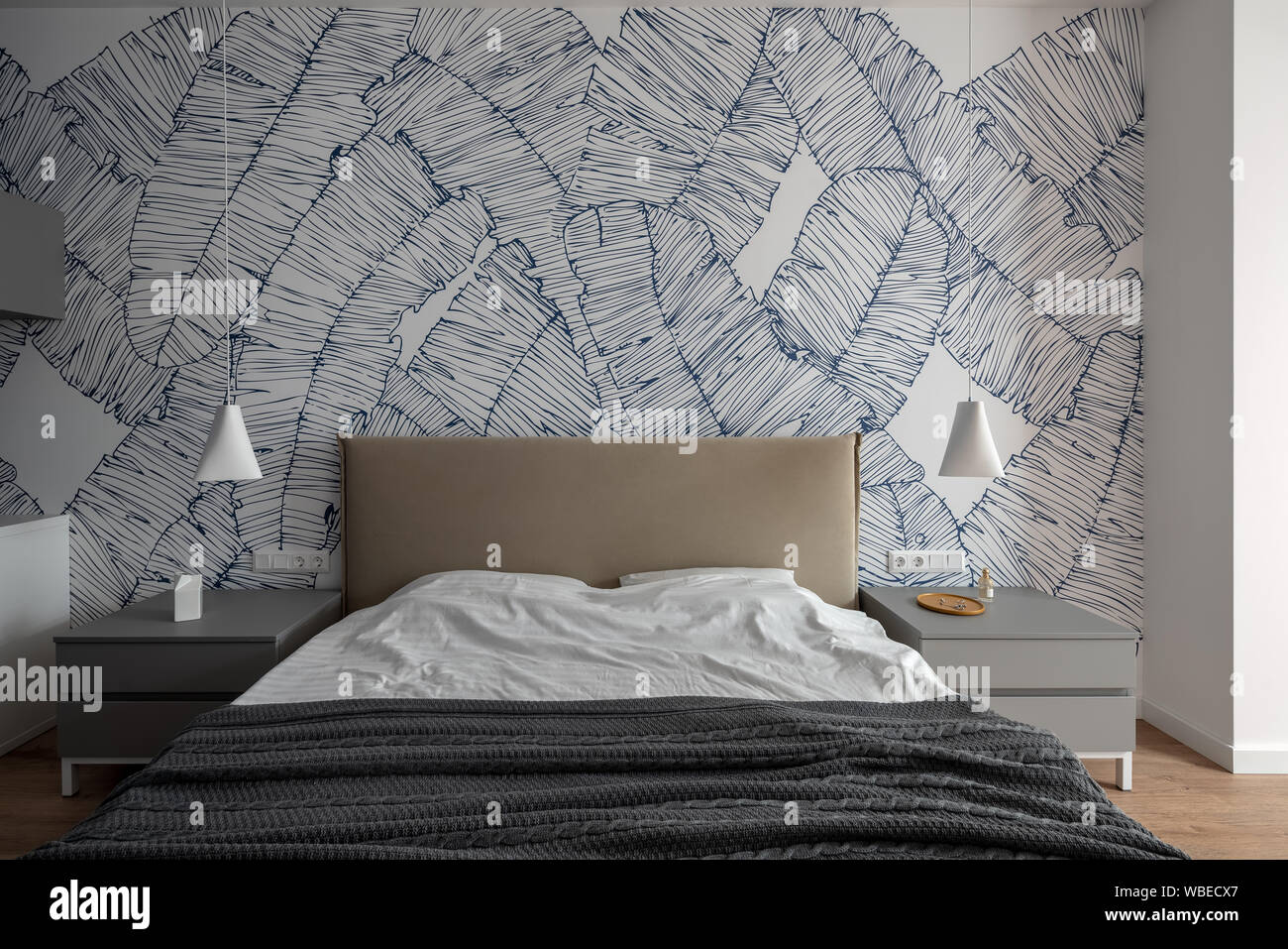 Camera da letto in stile contemporaneo con pareti bianche con modelli e un pavimento in parquet. Vi è un letto matrimoniale con biancheria chiara e scura coverlet, grigio notte Foto Stock