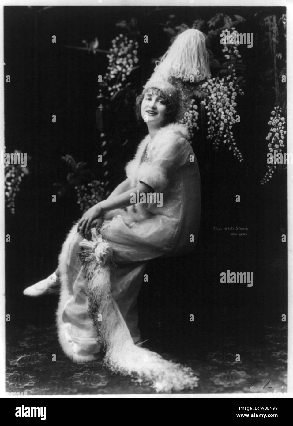 Gaby Deslys, 1884-1920, a piena lunghezza ritratto, seduto, rivolto leggermente verso sinistra in ornato hat e astratto del vestito/medio: 1 stampa fotografica. Foto Stock