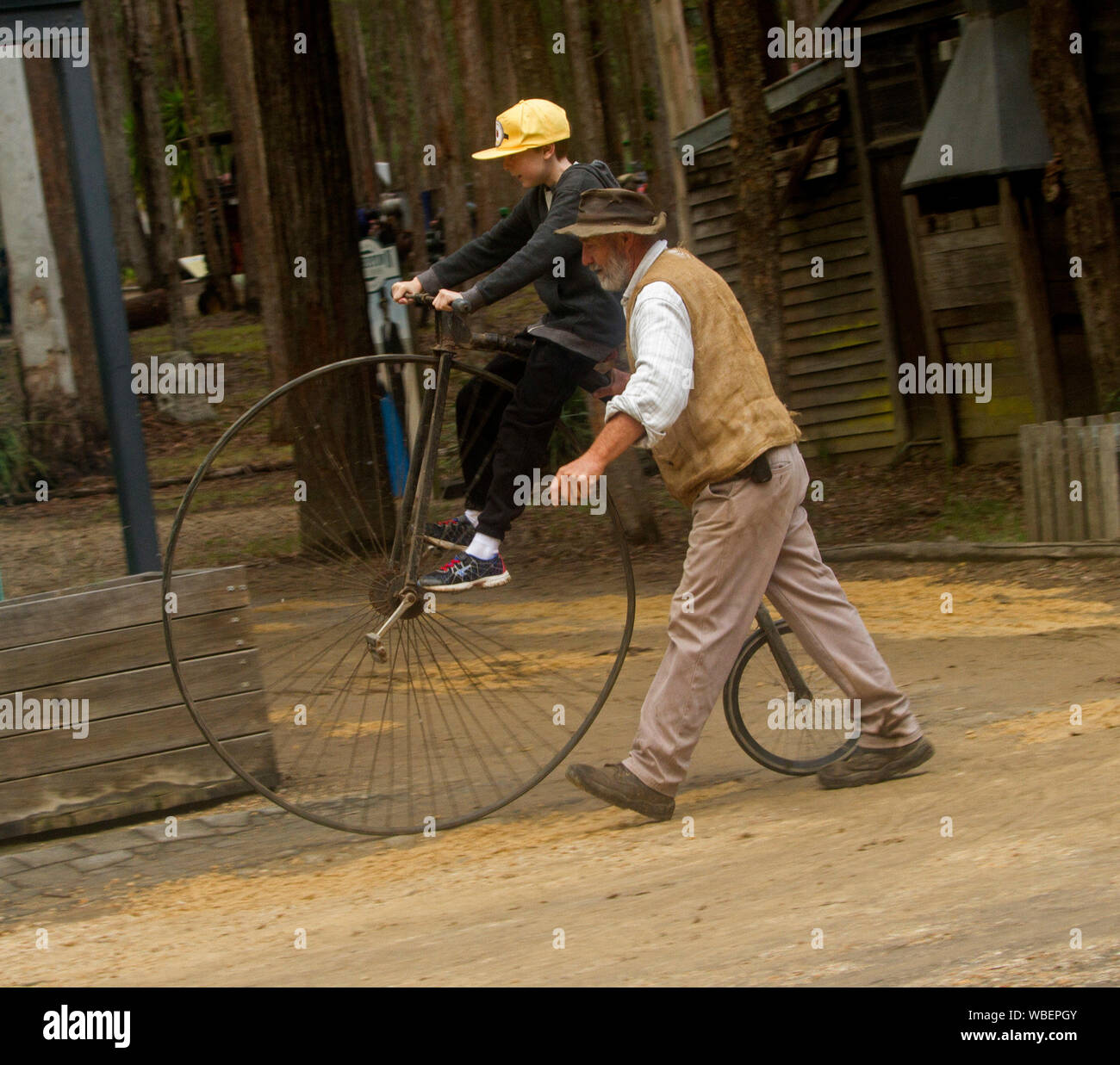 Uomo anziano aiutare i giovani ad un ragazzo a cavalcare un antico Penny Farthing bicicletta Foto Stock