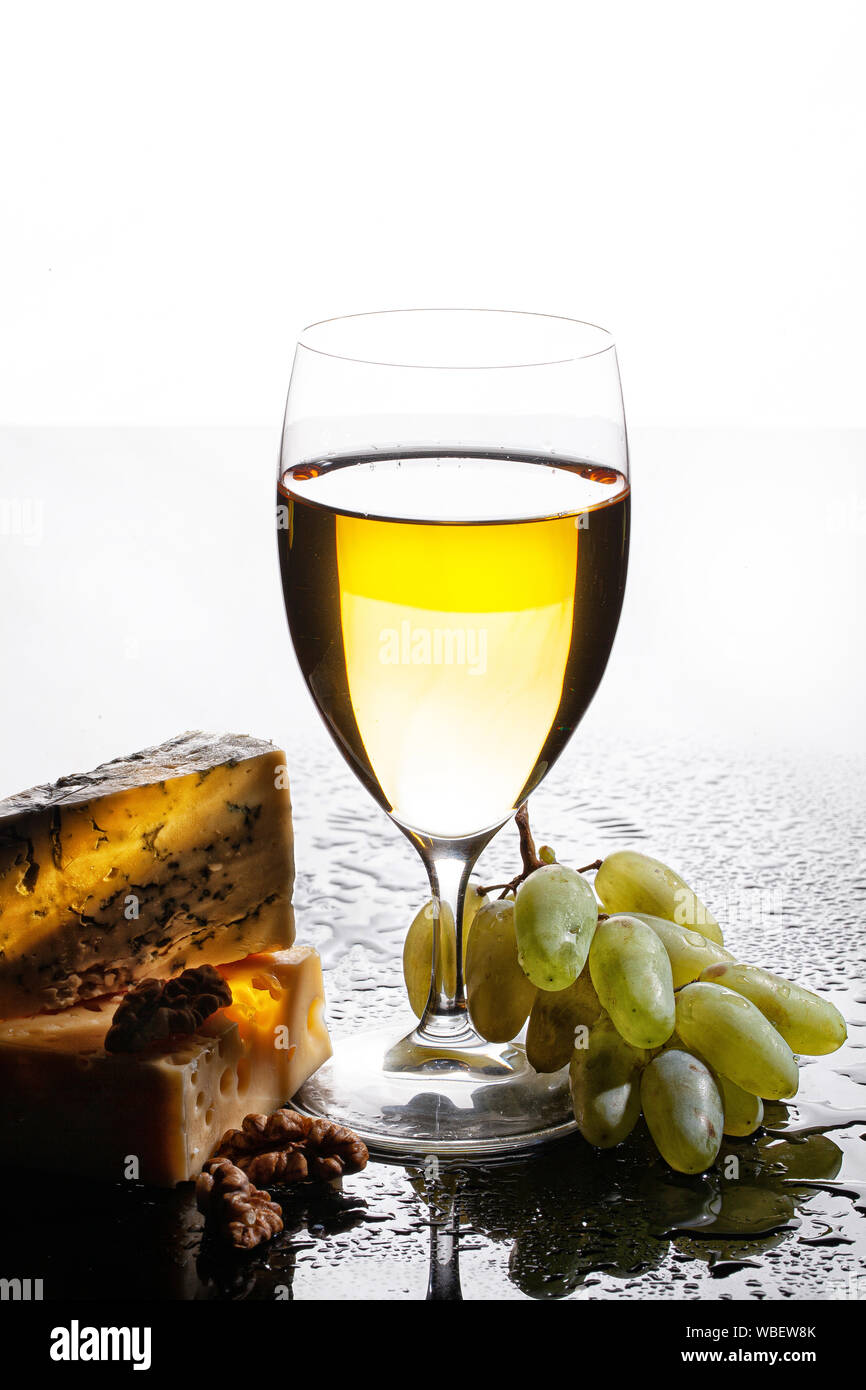 Bicchiere di vino, pezzi di formaggio e il grappolo di uva su un sfondo di vetro con gocce d'acqua Foto Stock