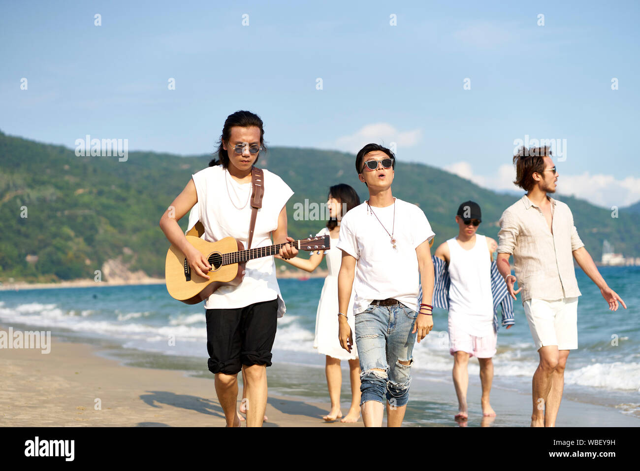 I membri di una rock band camminando sulla spiaggia a suonare la chitarra Foto Stock