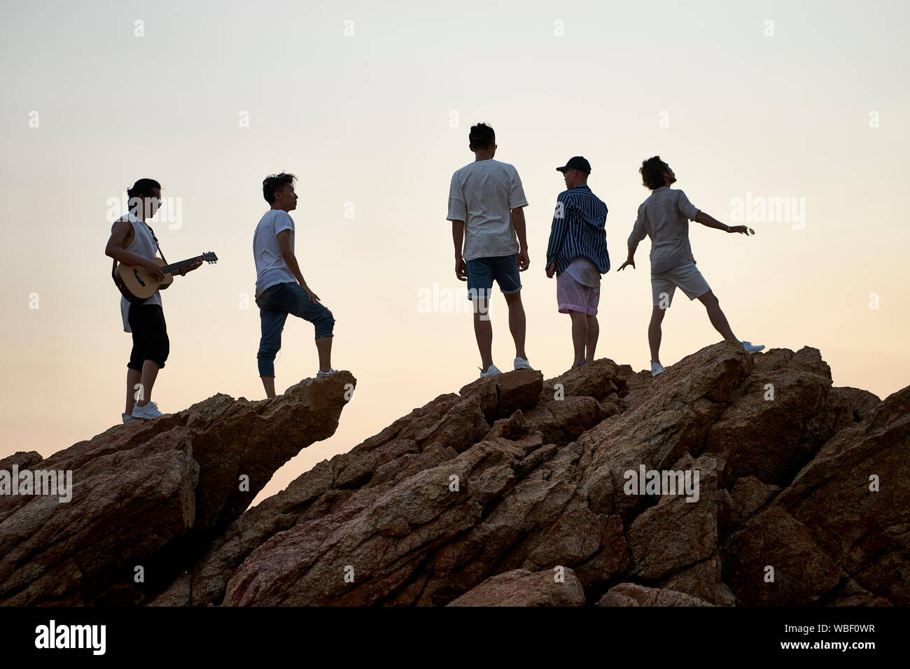 I membri di una rock band in piedi sulla parte superiore delle rocce in riva al mare a cantare a suonare la chitarra Foto Stock