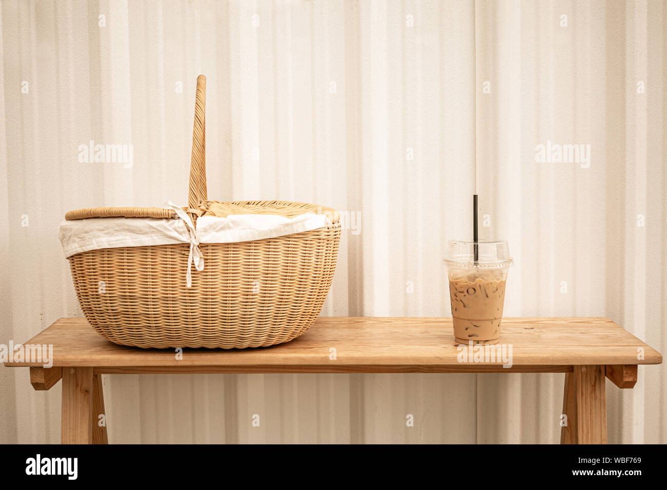 Iced frappucino miscelato in una tazza di plastica e Cesto picnic sulla panca di legno. Caffè ghiacciato. Vintage del tono di colore. Foto Stock