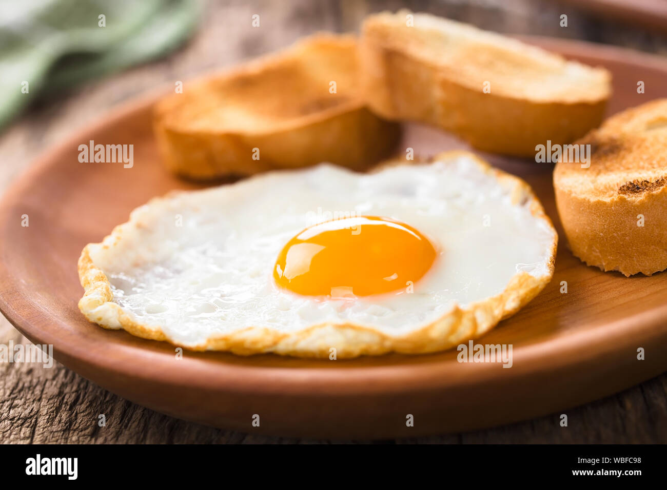 Una fresca uovo fritto sunny side up con baguette tostate fette sul lato servite sul piatto di legno (messa a fuoco selettiva) Foto Stock
