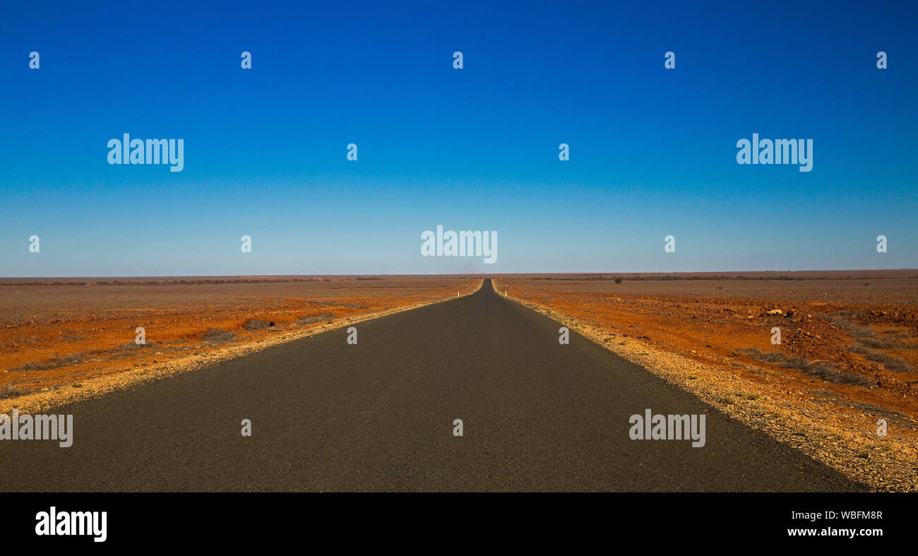 Diritta lunga strada di bitume che spazia su tutta la sterile red outback australiano pianure a lontano orizzonte sotto il cielo blu Foto Stock