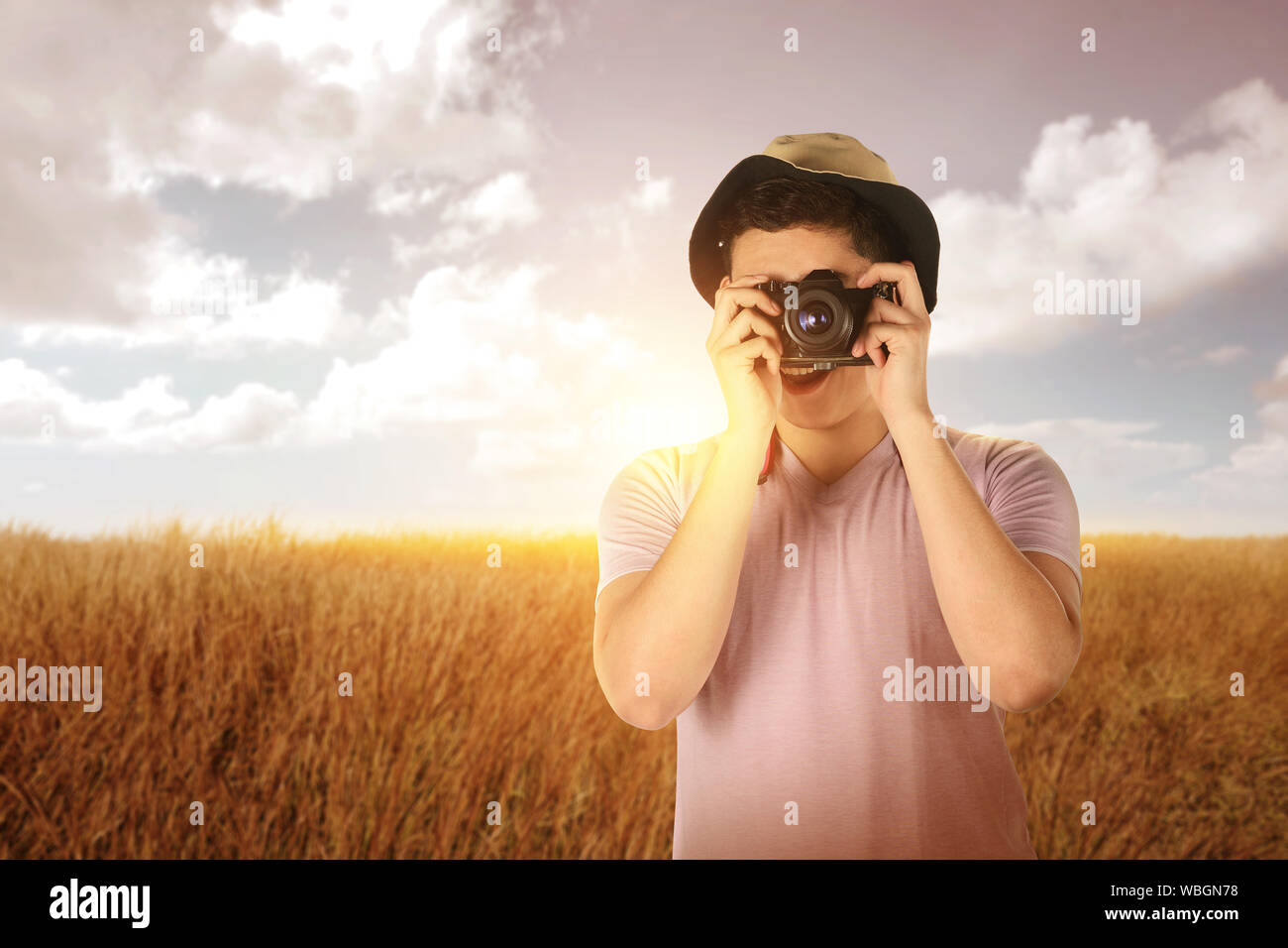 Uomo asiatico nella HAT di scattare una foto con la fotocamera sul campo in erba Foto Stock