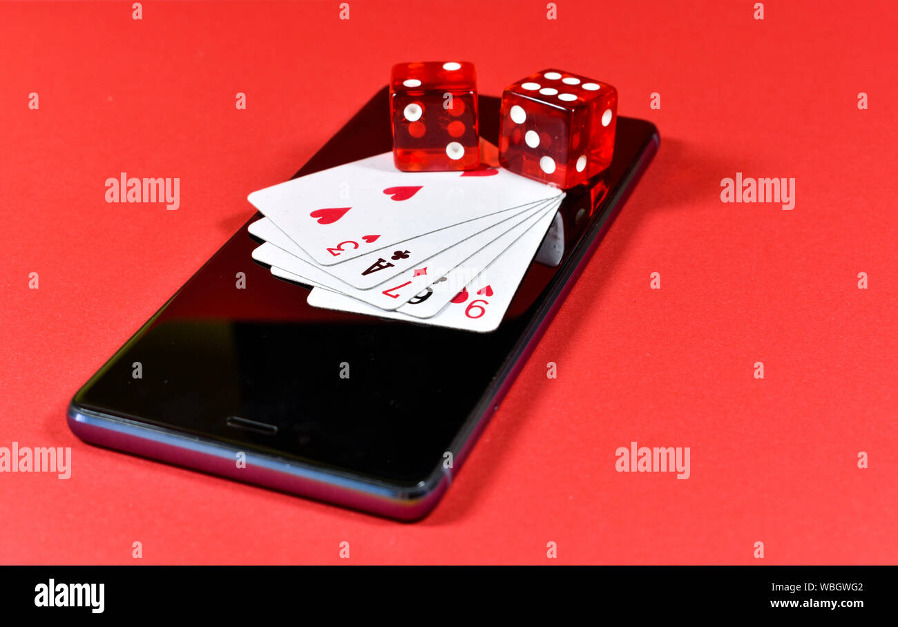 Mobile phone su sfondo rosso con diverse carte da gioco e dadi rossi sul display, immagine concettuale su mobile industria del gioco Foto Stock