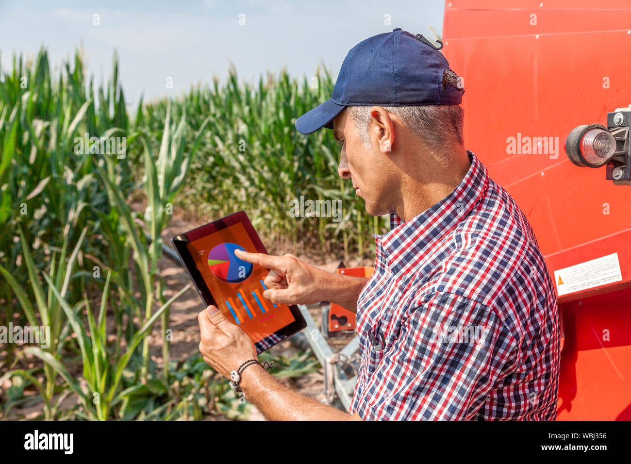 Moderno agricoltore tecnologico durante il controllo della crescita dei dati di mais sulla tavoletta del suo campi coltivati. concetto di uno sfruttamento sostenibile di natu Foto Stock