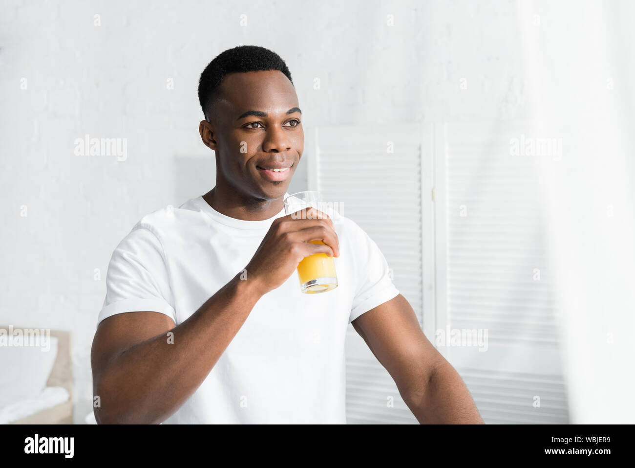 Felice African American uomo che guarda lontano e di bere succo di arancia Foto Stock