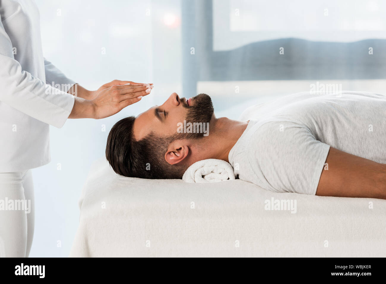 Vista ritagliata di guaritore mettendo le mani sopra la testa di uomo barbuto con gli occhi chiusi Foto Stock