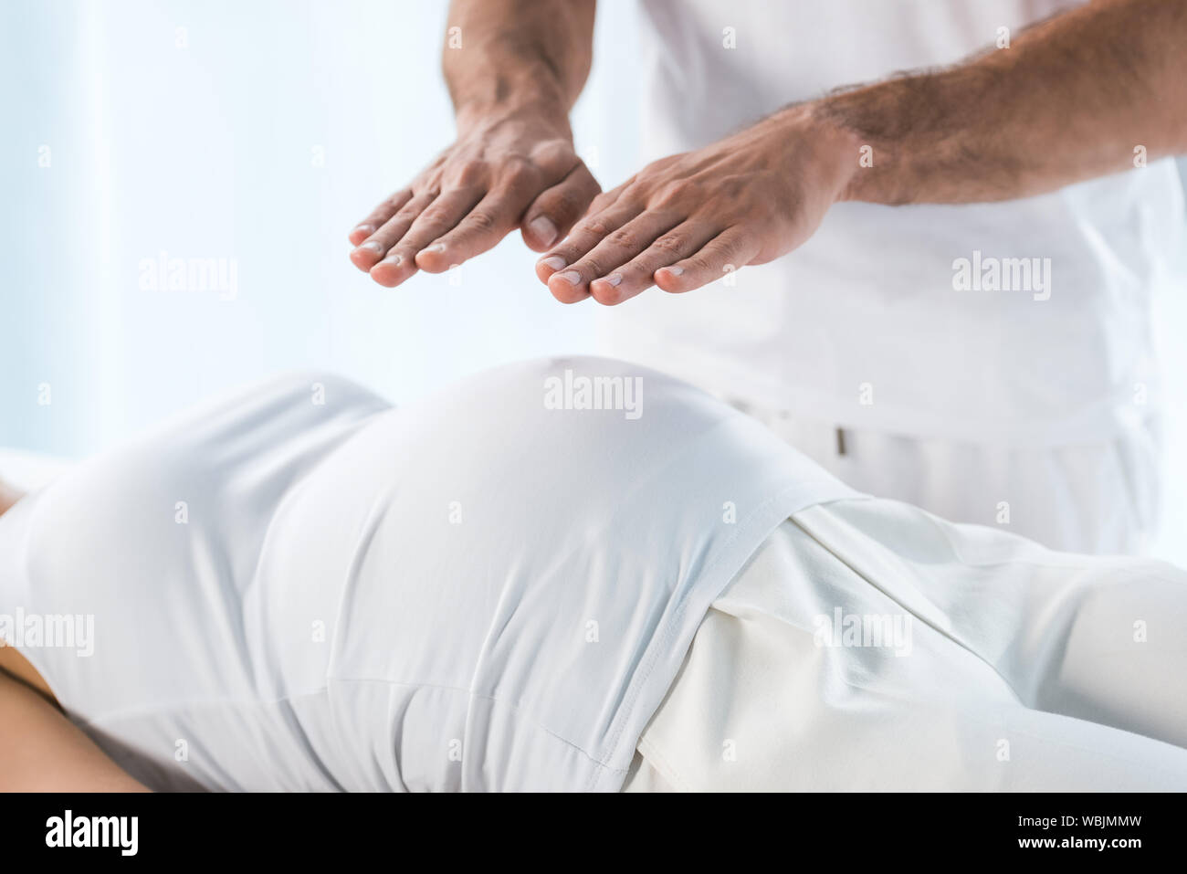 Vista ritagliata di guaritore mettendo le mani sopra la pancia della donna in stato di gravidanza Foto Stock