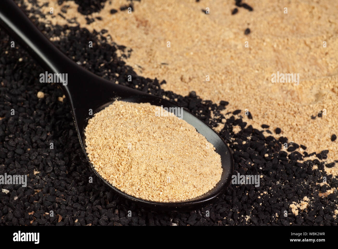 Lo zenzero in polvere in cucchiaio su nero semi di cumino sfondo. nigella sativa o kalonji Foto Stock