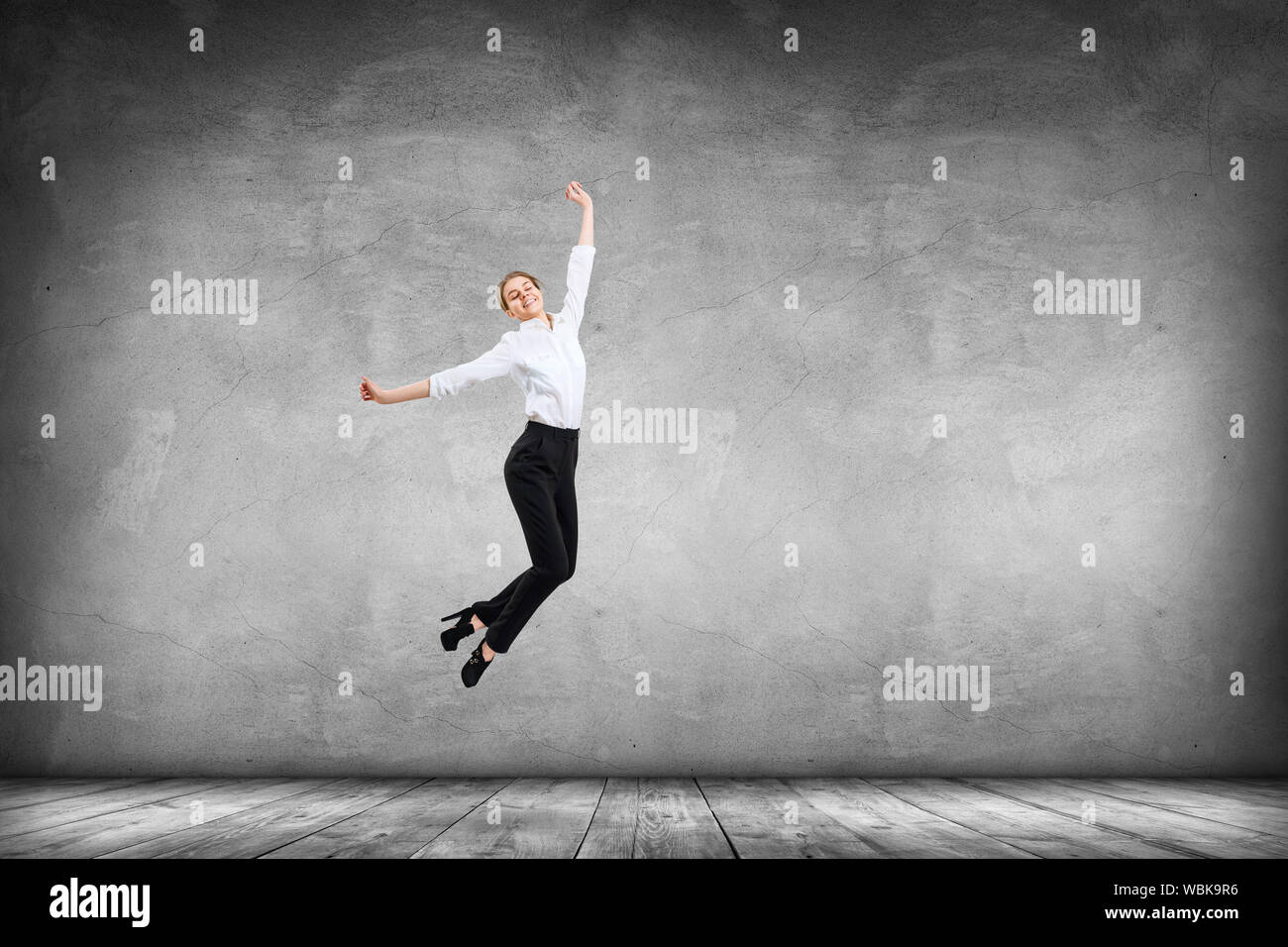 Felice giovane donna in abbigliamento formale salta verso l'alto. Oltre il muro grigio Sfondo. Foto Stock