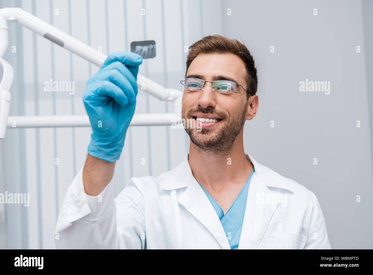 Messa a fuoco selettiva di allegro dentista in bicchieri azienda x-ray in clinica Foto Stock