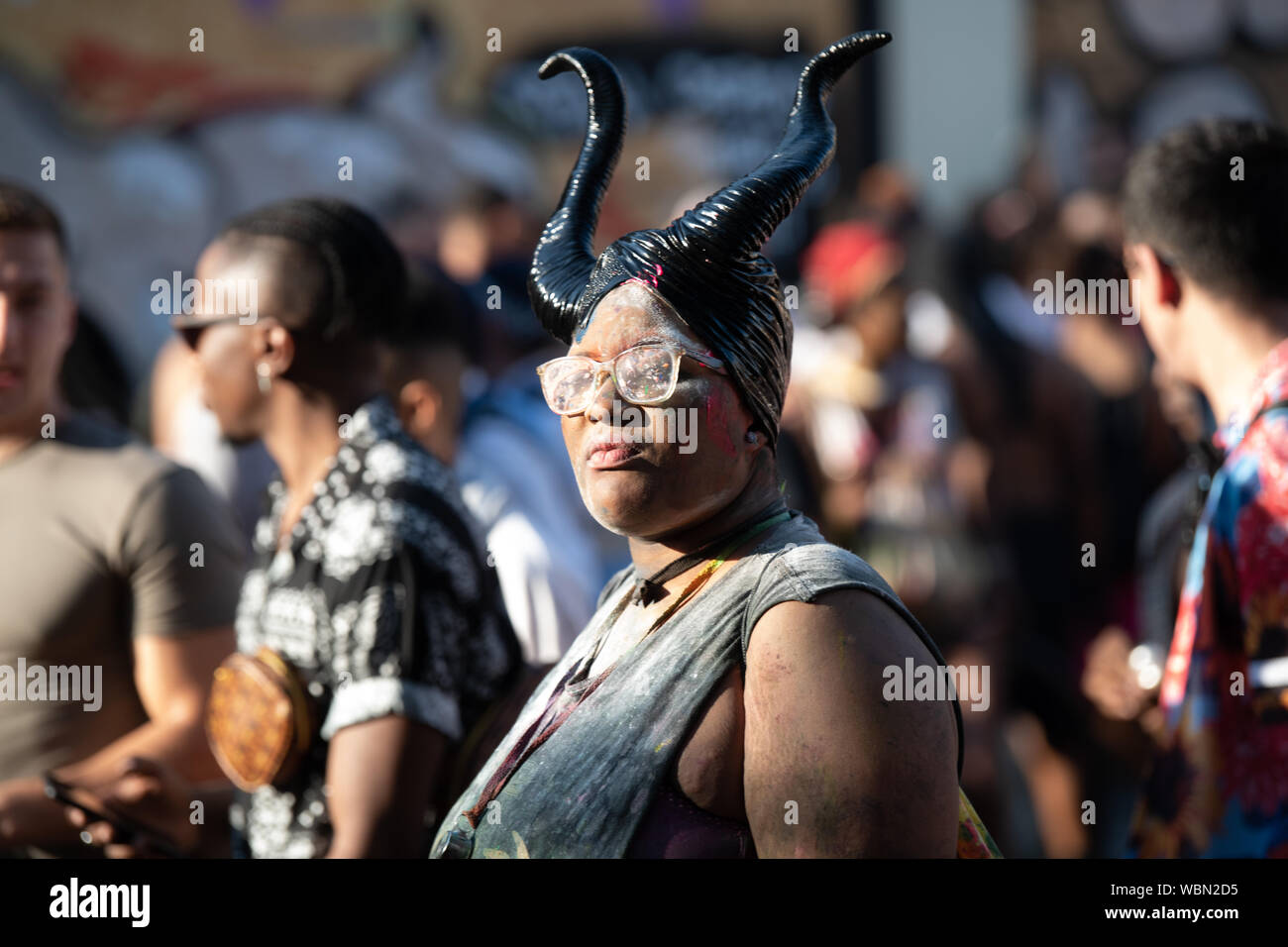 Una donna nera al carnevale di Notting Hill che indossa un set di corna e bicchieri. Foto Stock