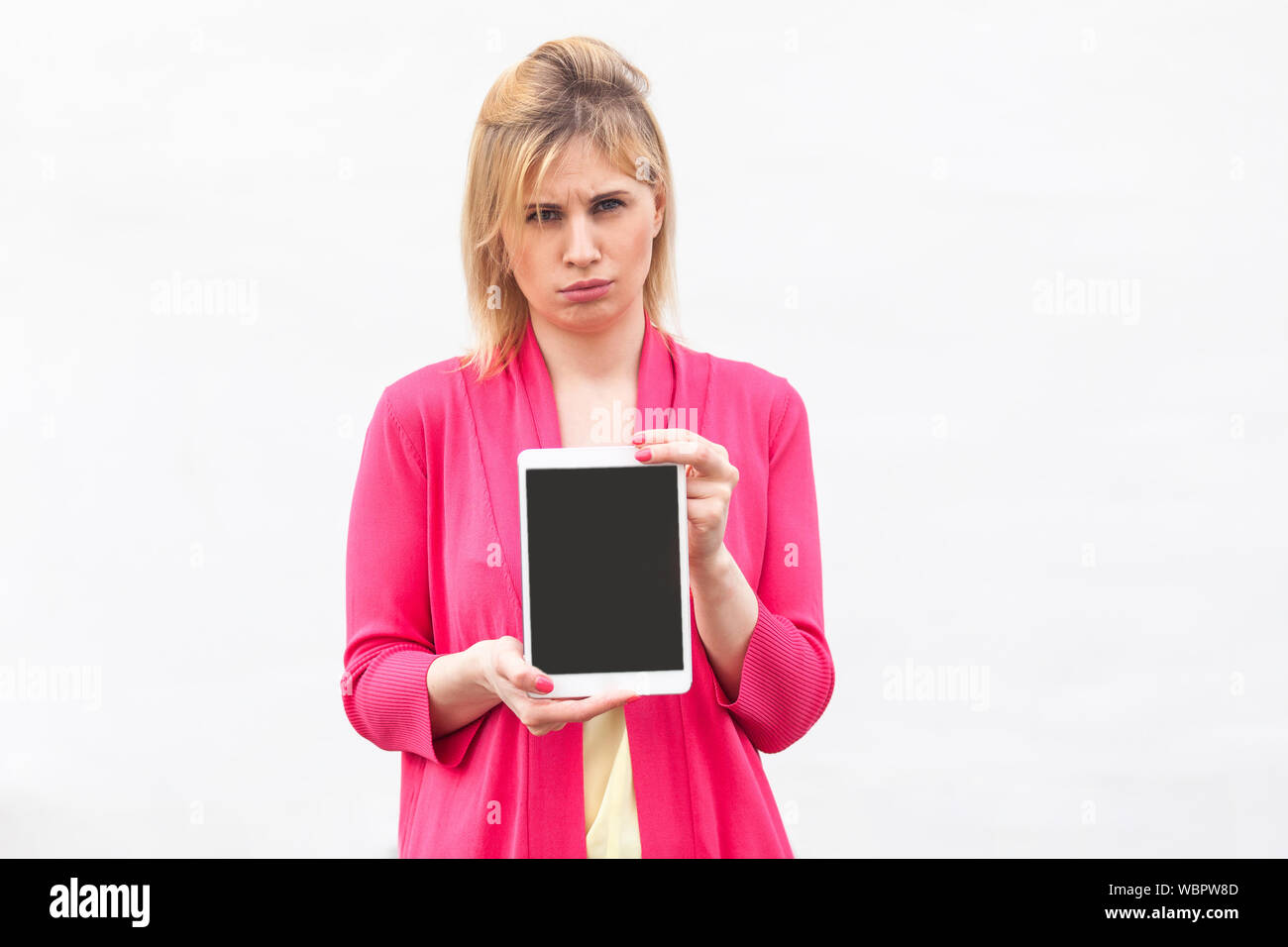 Ritratto di insoddisfatto bella giovane imprenditrice in rosa camicetta permanente e la holding tablet schermata vuota e guardando la fotocamera con la faccia triste Foto Stock