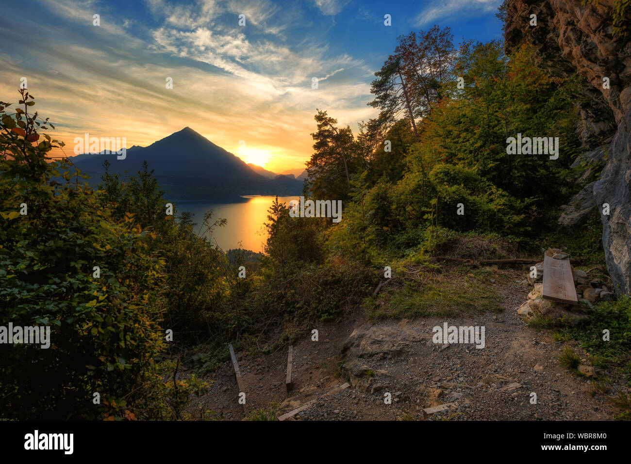 Banco di semplice sotto una roccia e oltre ad un percorso di montagna con vista sul lago di Thun al tramonto nel Simmental Foto Stock