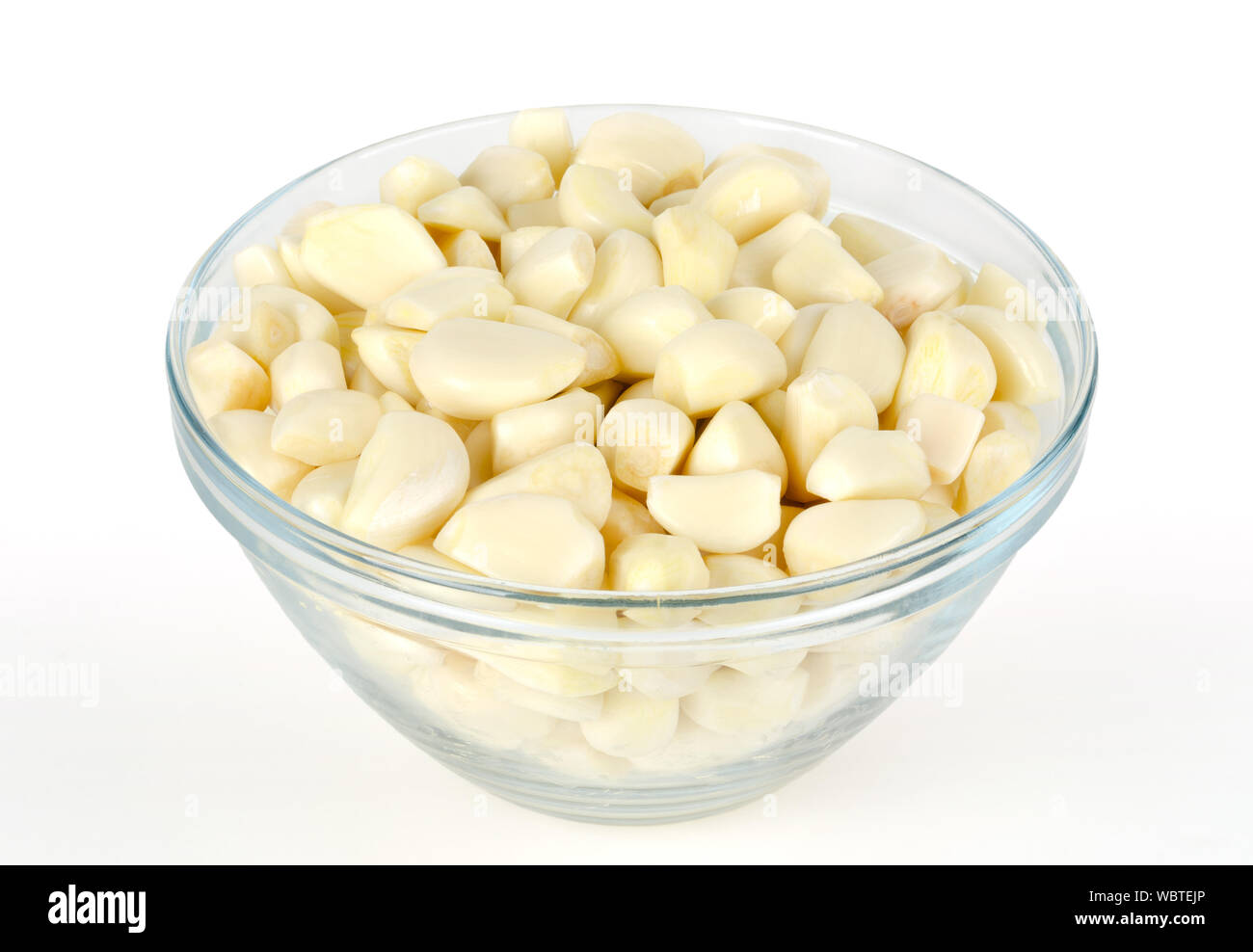 Spicchi di aglio sgusciati in recipiente di vetro, vista frontale. Allium sativum, con sapore pungente, usato come condimento o condimento e in medicina. Foto Stock