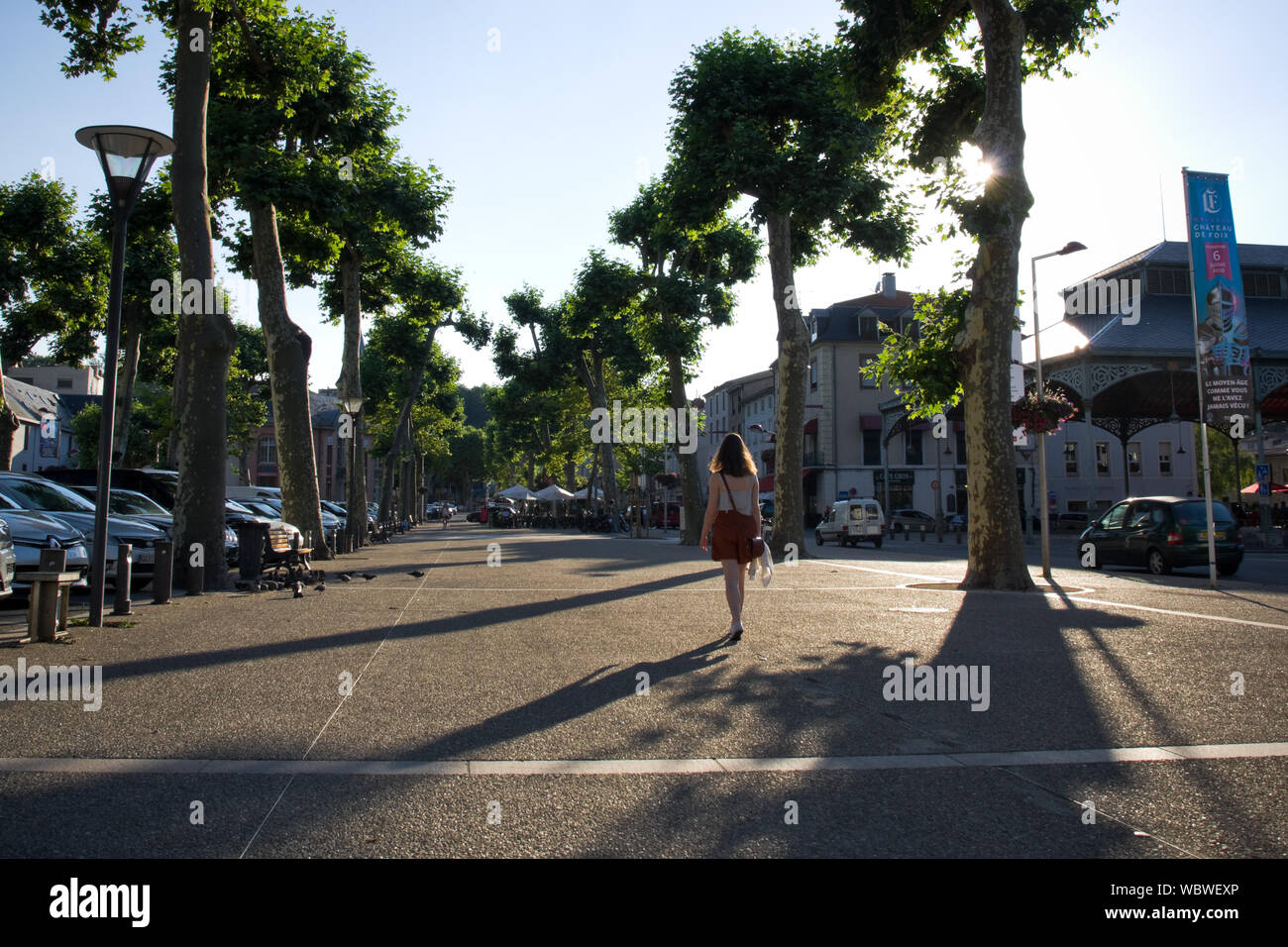 Una donna getta un'ombra sulla strada come lei cammina attraverso la città di Foix in serata. Ariège, il sud della Francia. Foto Stock