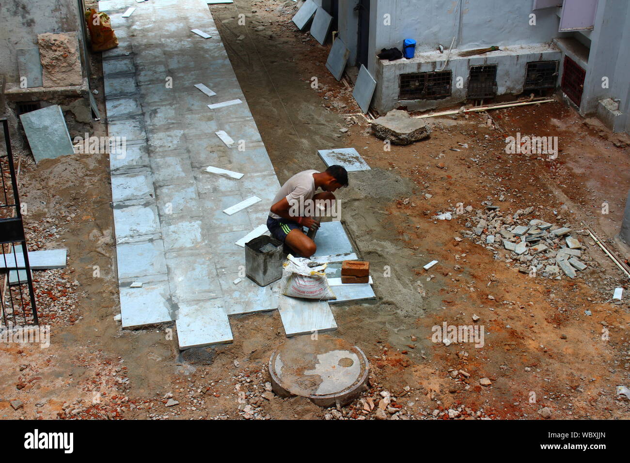 Lavoratore la posa di piastrelle in pietra sul pavimento esterno in un alloggiamento della società in Delhi, India Foto Stock