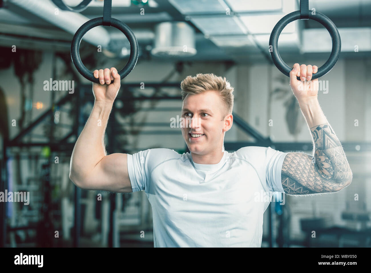 Bel giovane con forti braccia appeso su anelli di ginnastica in palestra Foto Stock