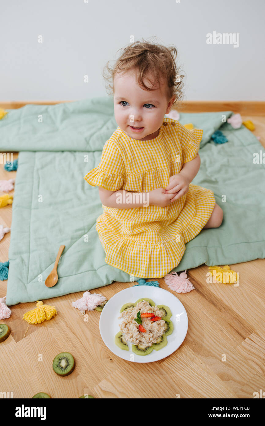 Molto carino il bambino mangiare i fiocchi d'avena con kiwi Foto Stock