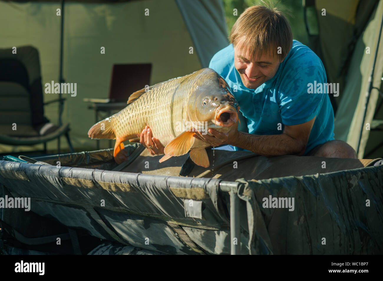 Fisherman sorriso con la carpa in accampamento di pesca Foto Stock