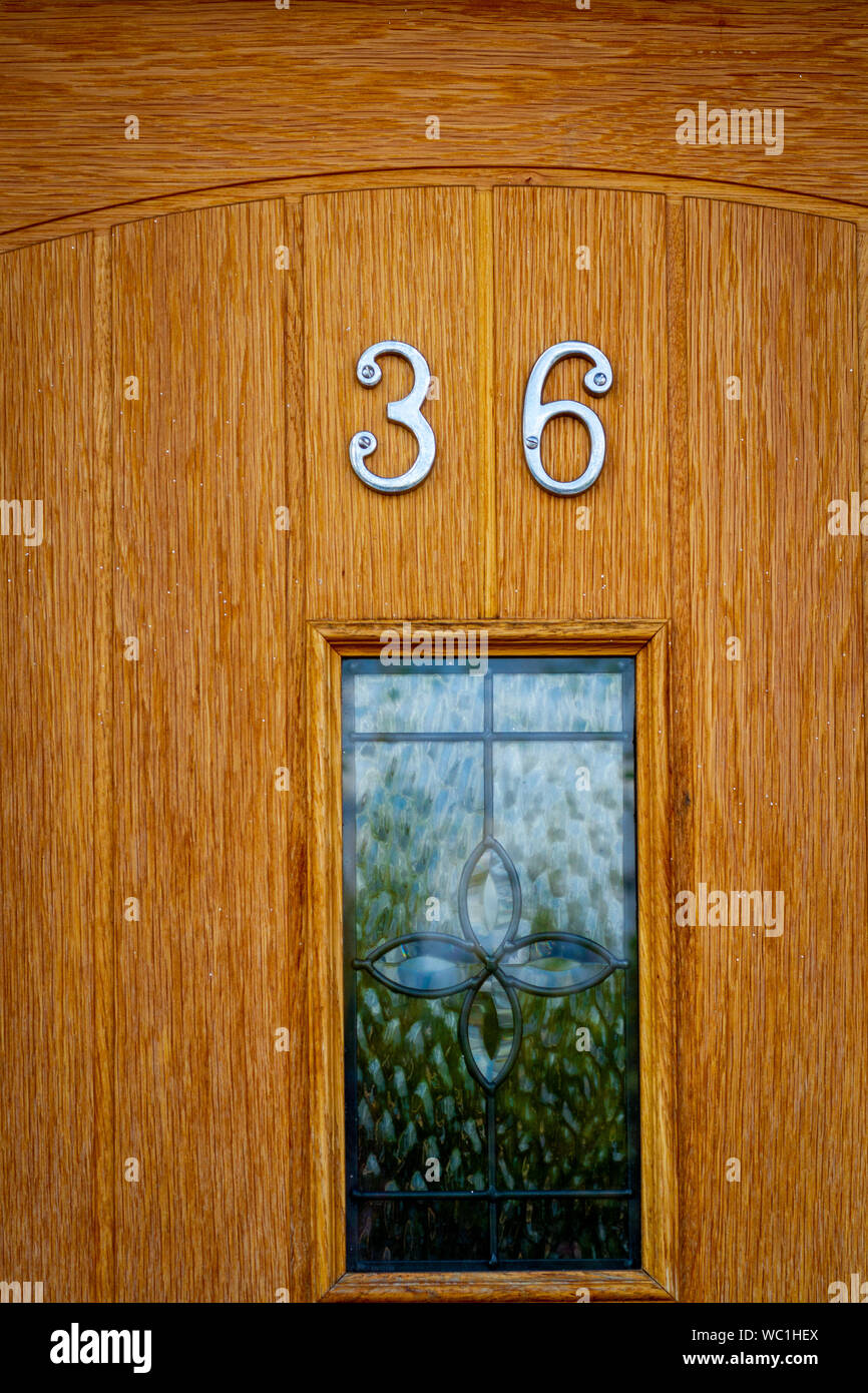 Il numero civico 36 su una grana naturale e verniciato porta in legno tinto con inserto in vetro Foto Stock