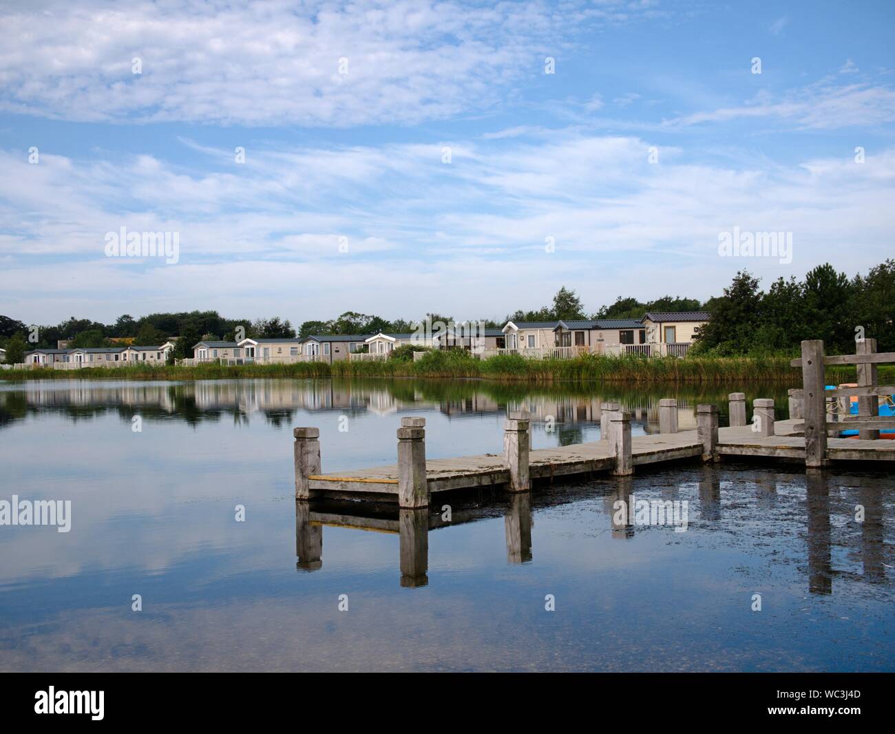 Pontile in legno sul lago con canne lungo la riva e vacanze roulotte e ombre Foto Stock