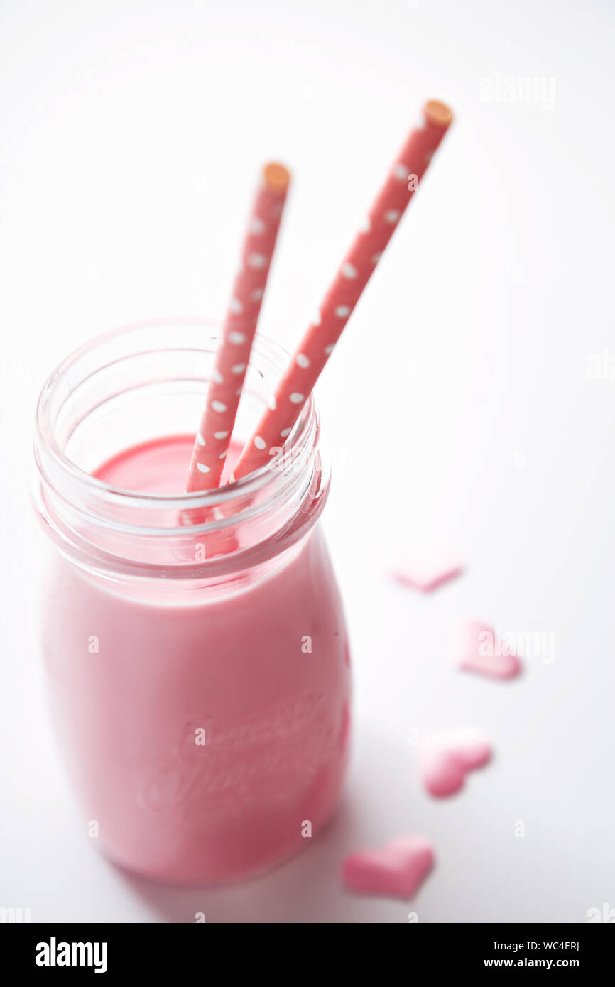 Close-up di confettura di lamponi frullati in vaso con cannucce rosa contro uno sfondo bianco Foto Stock