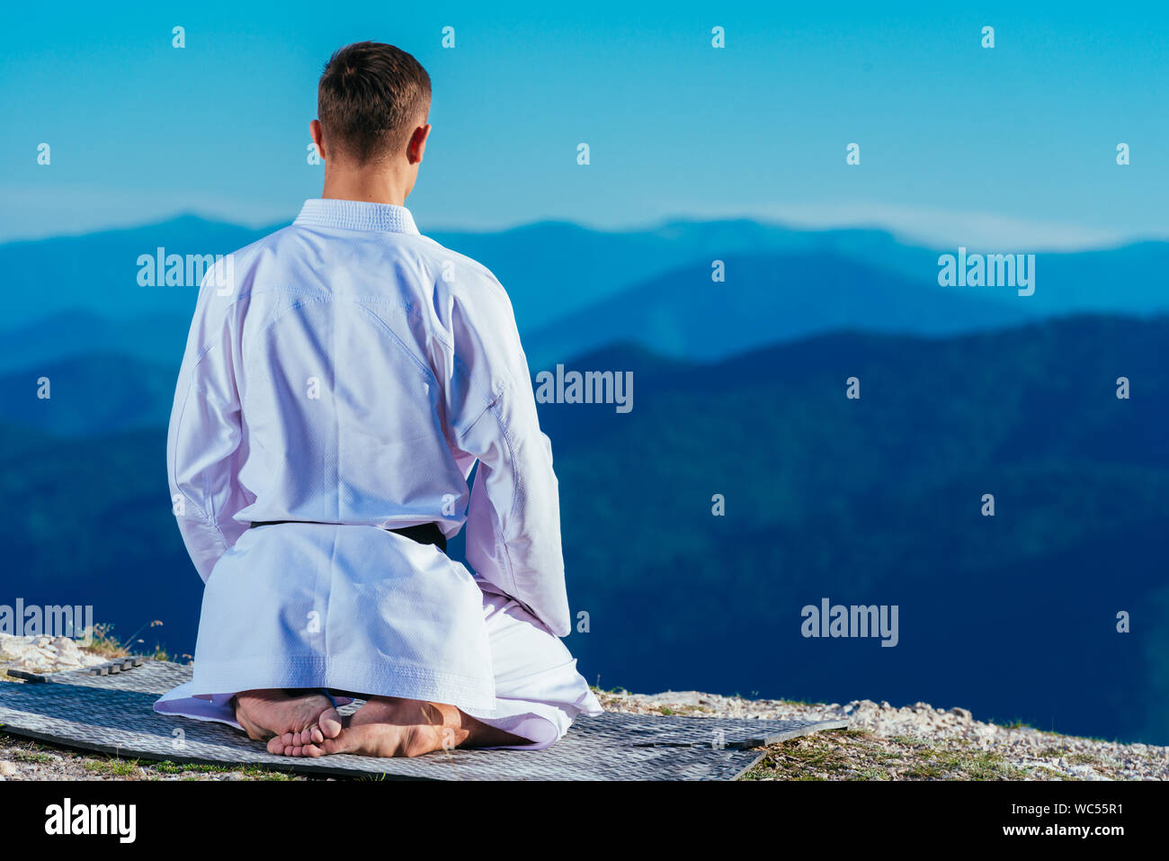 Karate master meditando sulla cima di una montagna di indossare il kimono mentre guardando giù al lago di montagna. Foto Stock